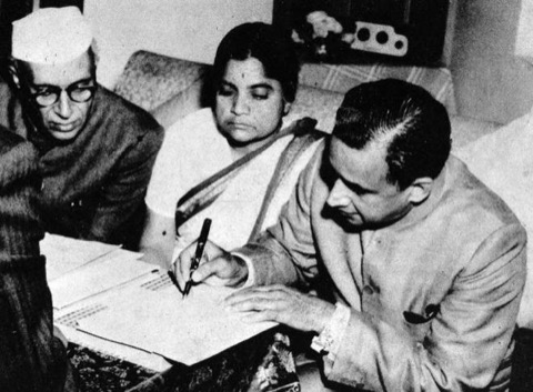 Durgabai Deshmukh seated between two men as a document is signed.